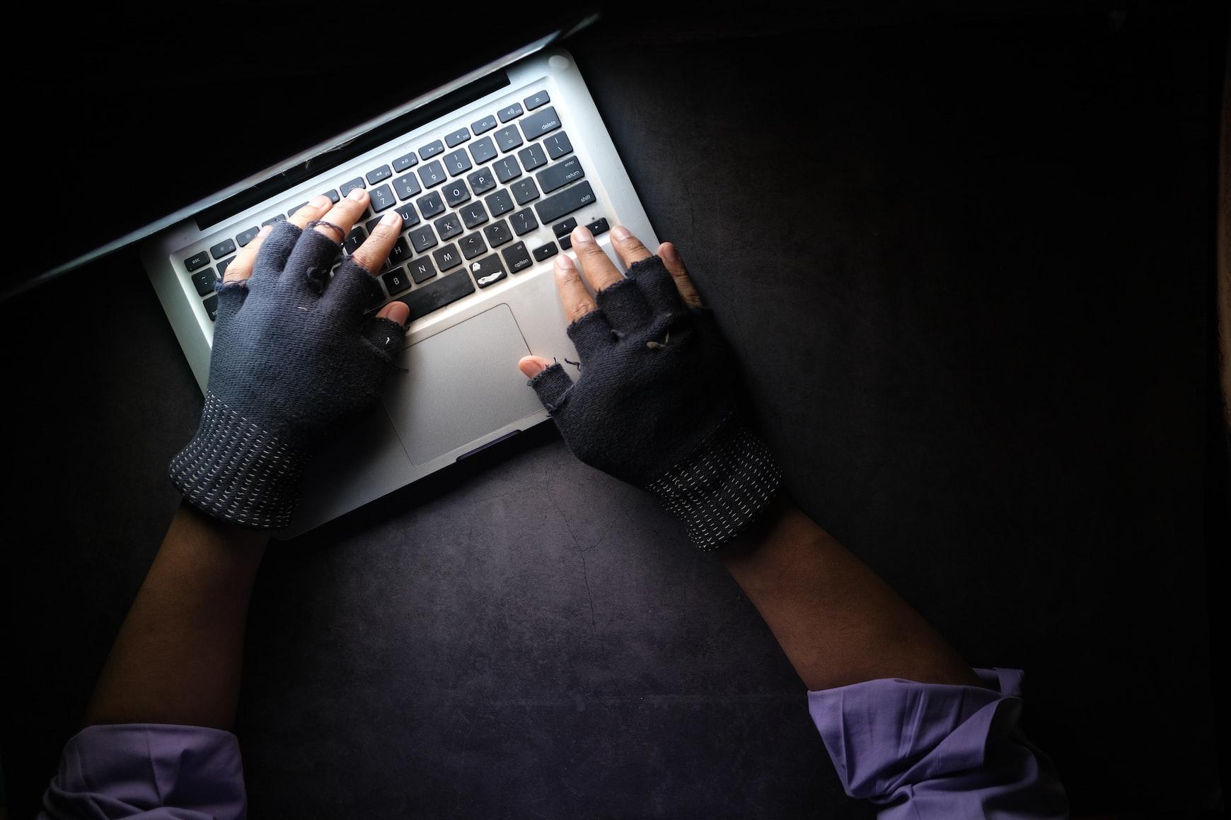 A person wearing black gloves using a MacBook