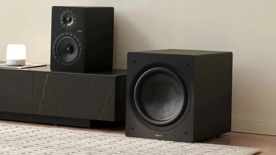 Black Elipson subwoofer beside a media cabinet topped by a matching bookshelf speaker